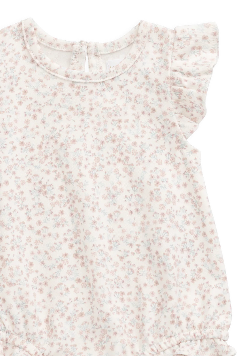 A close-up of a baby romper or long-sleeve top with a delicate, all-over small floral print in soft pink and light blue on an off-white background. It features ruffled cap sleeves and a round neckline.