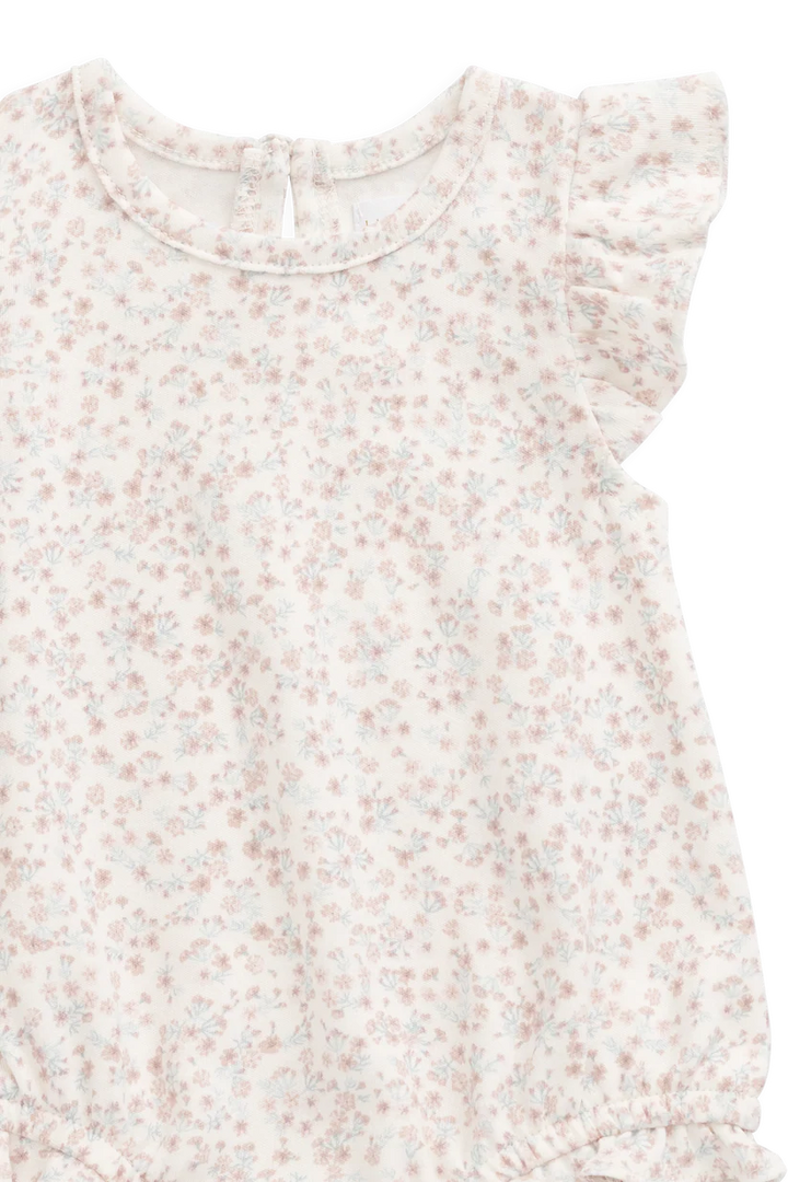 A close-up of a baby romper or long-sleeve top with a delicate, all-over small floral print in soft pink and light blue on an off-white background. It features ruffled cap sleeves and a round neckline.