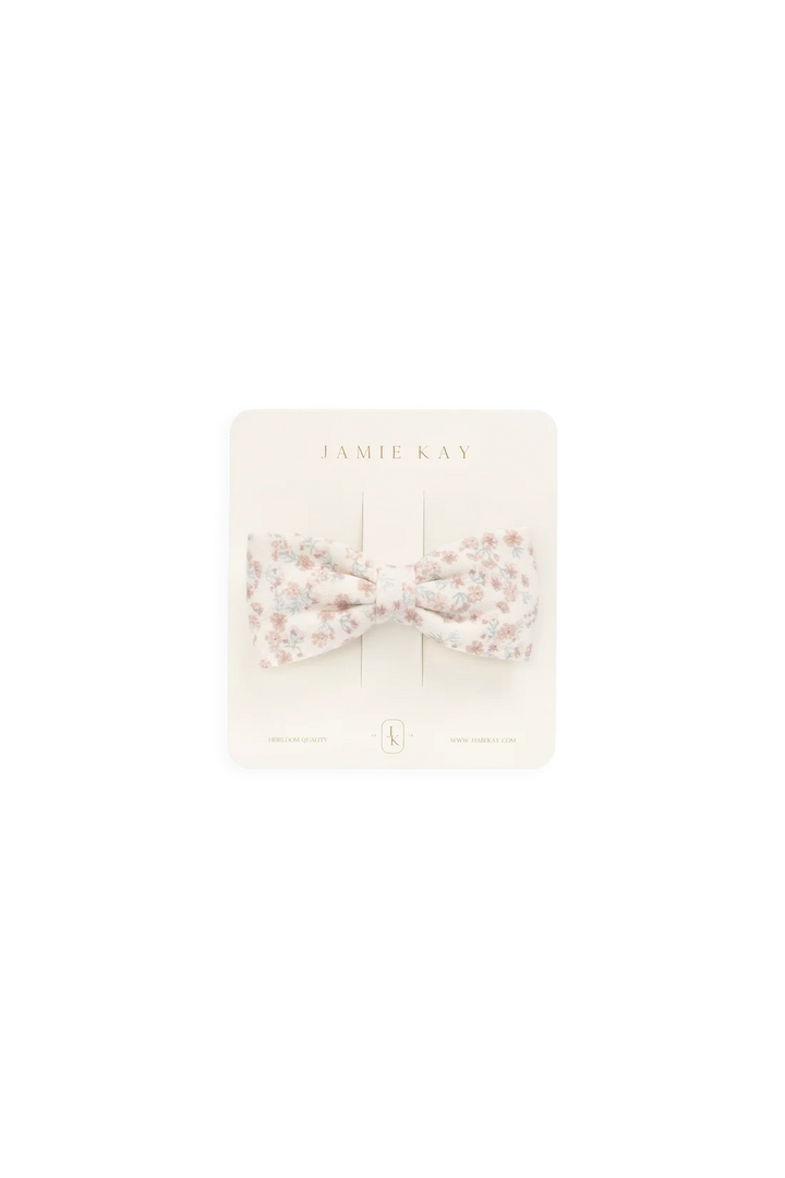 A small bow-shaped hair accessory with a delicate floral print in soft pink, beige, and white, presented on a cream-colored display card labeled 'JAMIE KAY'.