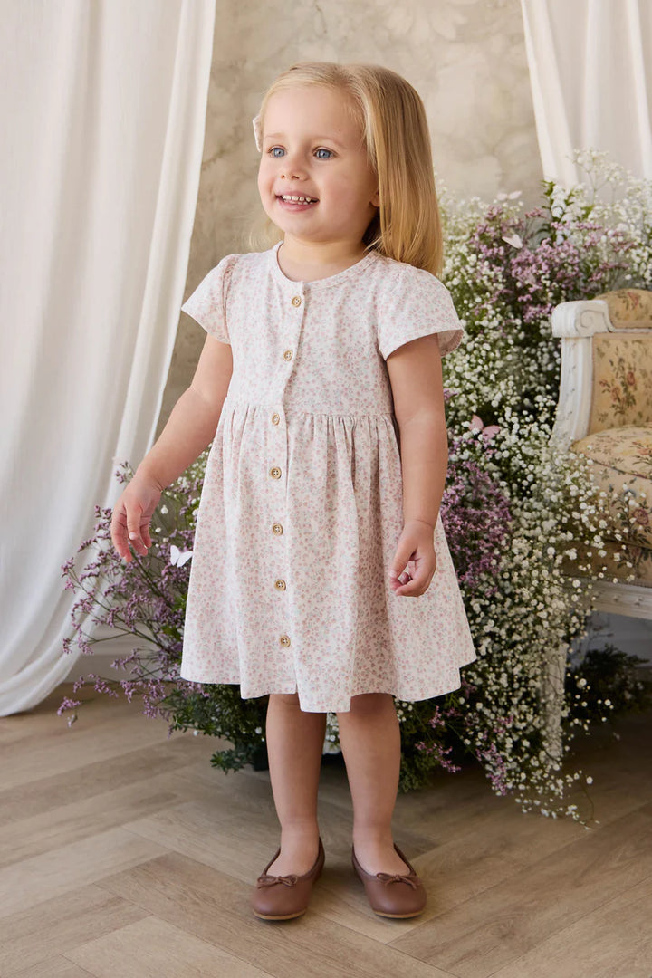 Young girl in a white floral dress standing in a decorated room with flowers and a chair.
