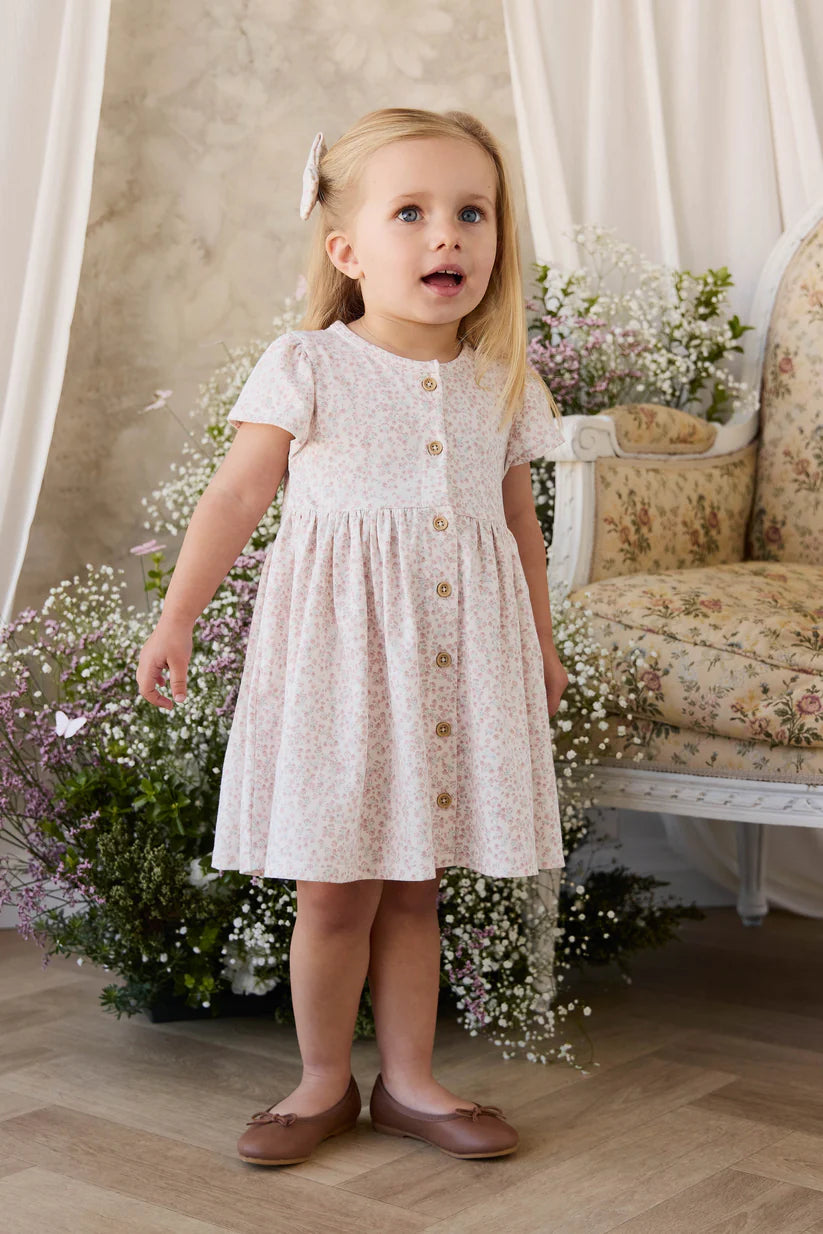 Young girl in a white floral dress standing in a decorated room with flowers and a sofa.