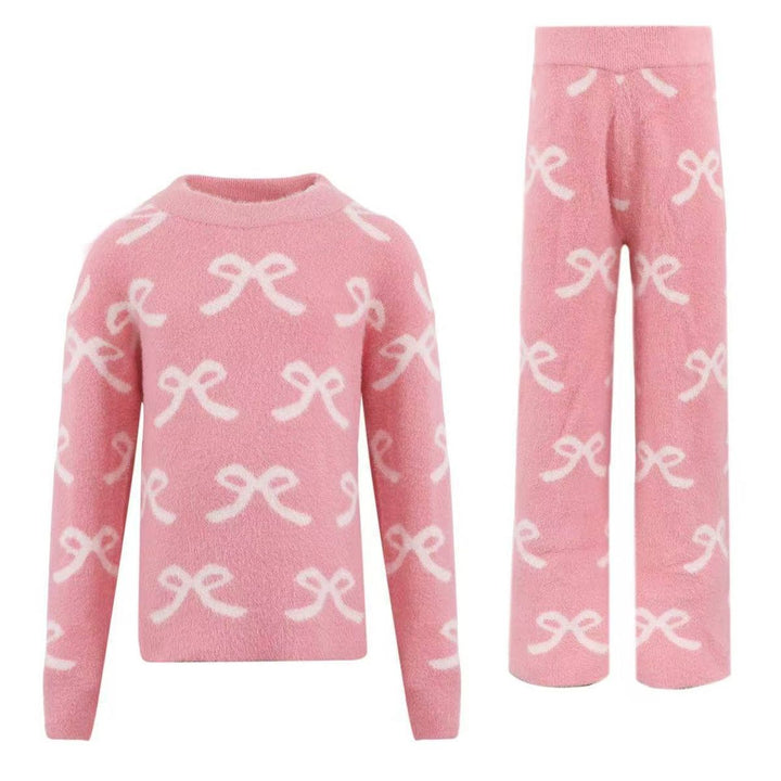 A two-piece children's sweater set in pink fleece, featuring a long-sleeve top and matching pants, both decorated with a white knit bow pattern, shown against a plain white background.
