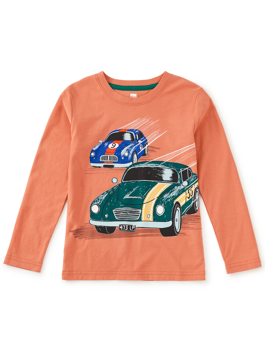 A children's long-sleeve t-shirt in a warm peach-orange color, featuring a graphic print of two vintage racing cars (a green MG with yellow stripes and a blue sports car) on a white background.