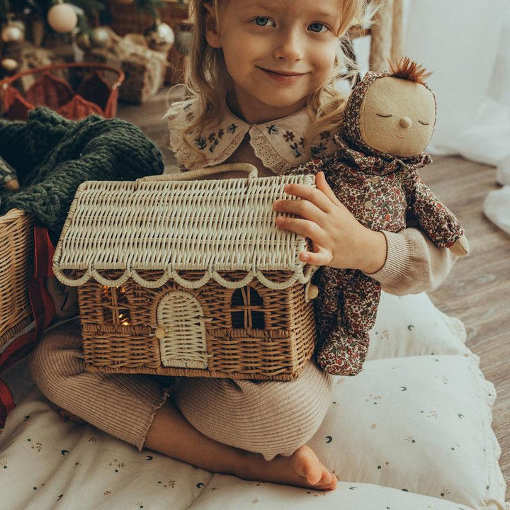 little girl holding baby doll and rattan doll house