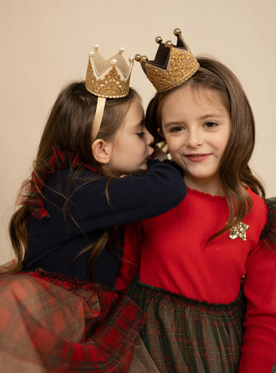 2 little girls wearing holiday dresses. One girl is wearing a dress with a red top and black plaid bottom and one girl is wearing a dress with navy top and red plaid bottom. 