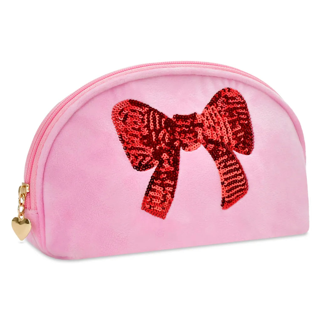 A pink velvet cosmetic pouch with a large red sequined bow on the front, featuring a gold zipper and a small gold heart charm.