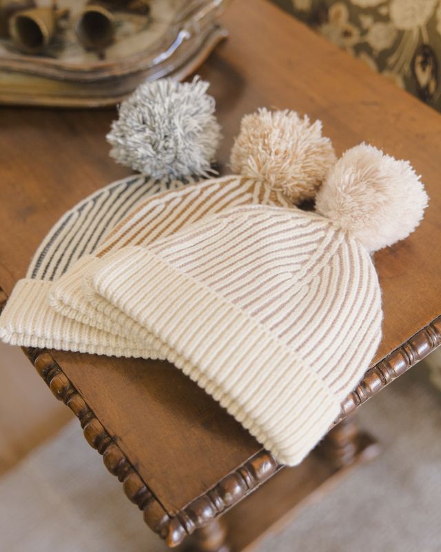 Three knit hats with pom-poms on a wooden surface