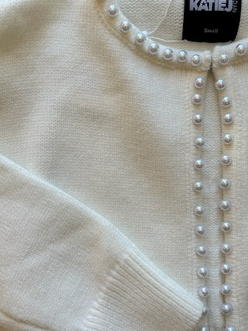 Close-up of a cream-colored cardigan with pearl embellishments and a visible brand label.