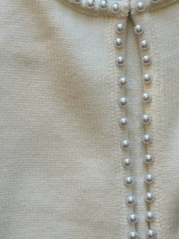 Close-up of a beige garment with pearl buttons on a neutral background