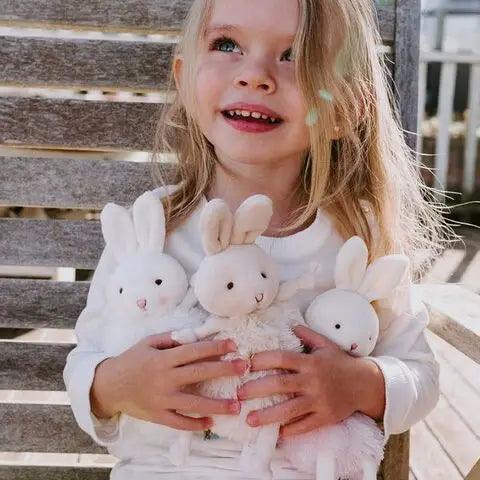 picture of a little girl holding 3 stuffed animal roly poly bunnies. 