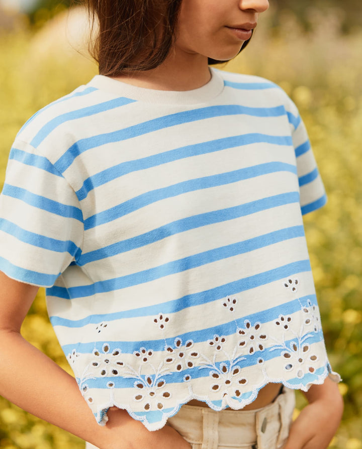 Person wearing a white and blue striped shirt with floral lace details in a blurred outdoor setting