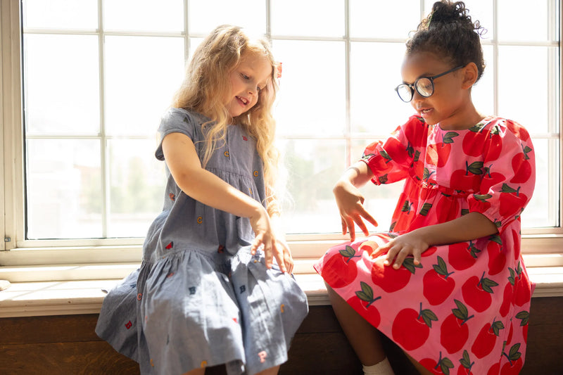 Two little girls sitting in a school library.  One of the little girls is sitting in the Rowan dress. 