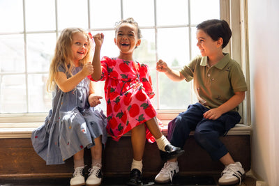 3 small children sitting in a window sill at the library in school clothes. The Rowan dress is featured here. 