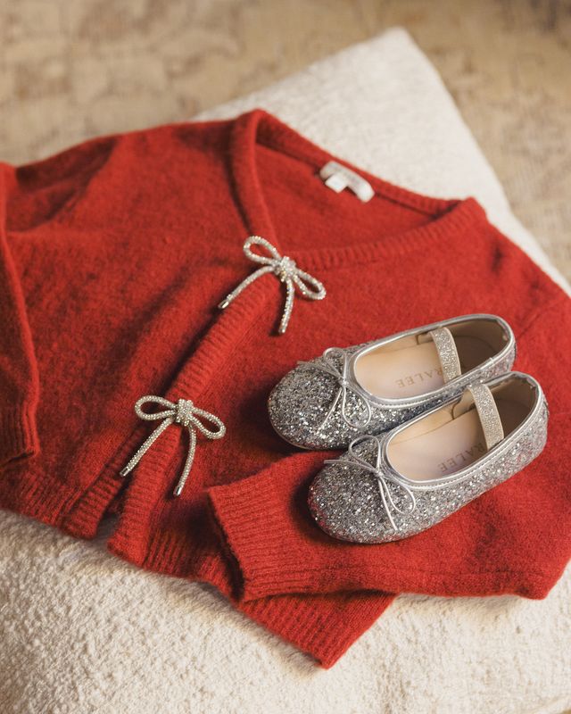 Red sweater with rhinestone bow buttons  and silver glittery shoes on a beige surface