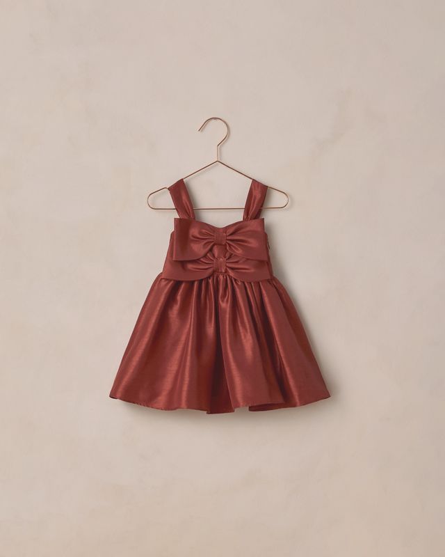 Red dress with a bow detail on a beige hanger against a beige background