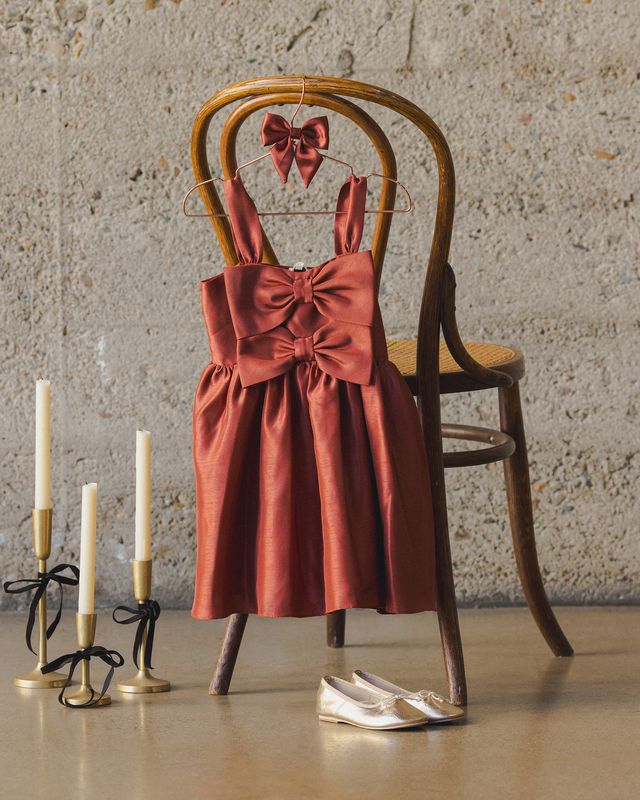 Red dress with a bow on a wooden chair against a textured wall.