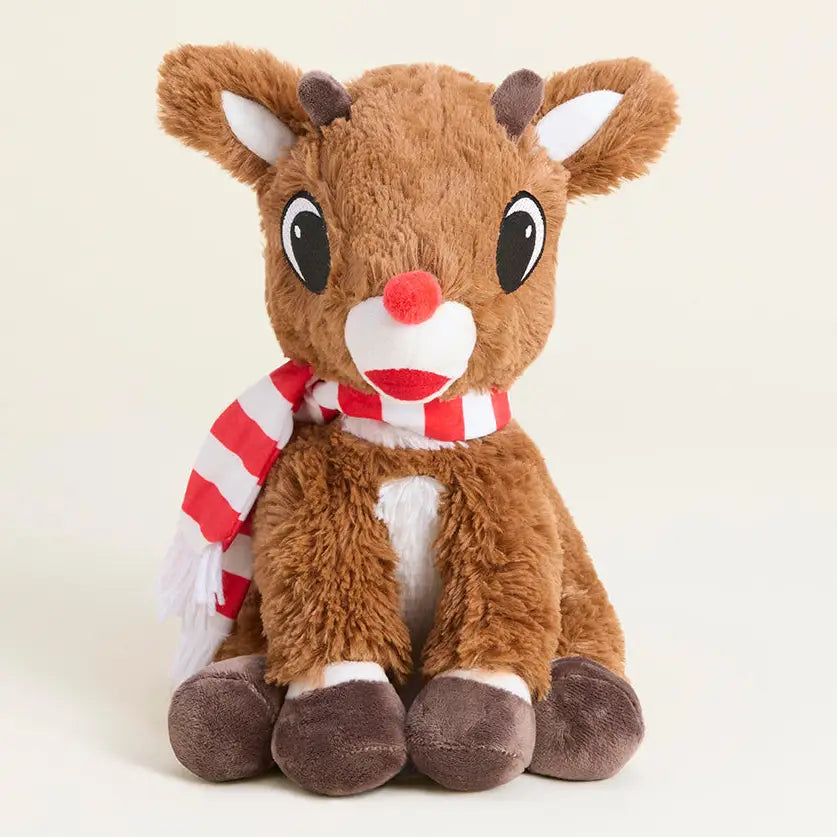A plush toy reindeer sitting upright, with brown fur, large black eyes, a red nose, a red-and-white striped scarf, and white inner ears and chest details, photographed on a clean light beige background.