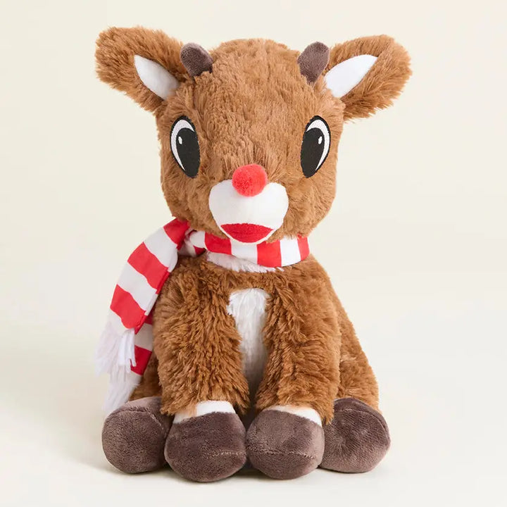 A plush toy reindeer sitting upright, with brown fur, large black eyes, a red nose, a red-and-white striped scarf, and white inner ears and chest details, photographed on a clean light beige background.
