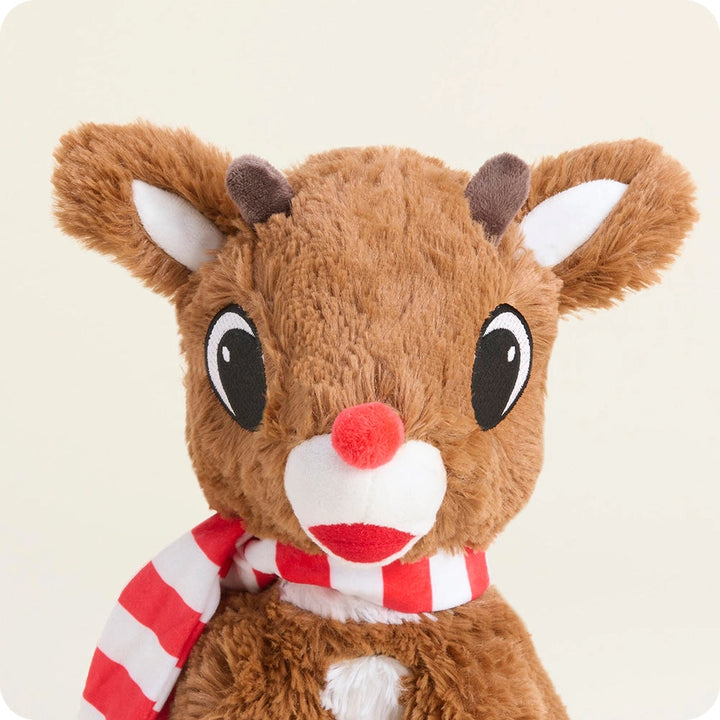 A plush toy reindeer with brown fur, large black eyes, a red nose, and a red-and-white striped scarf, photographed against a plain light beige background.