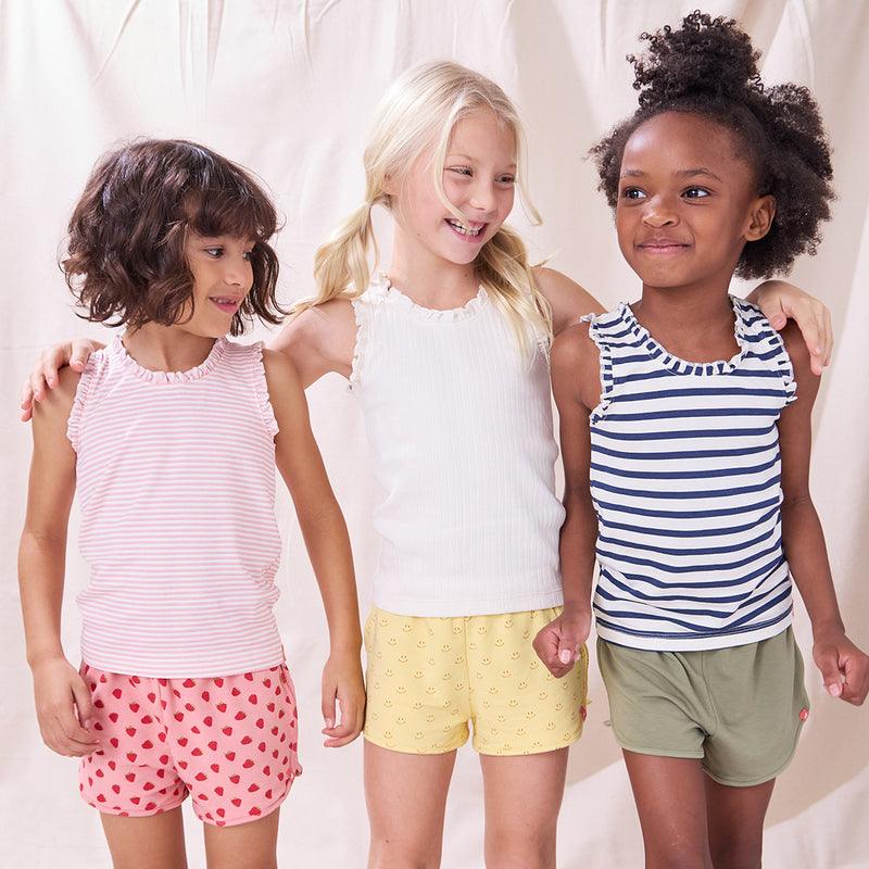 three young girls wearing the same cotton tank, 2 of them are striped one of them is ivory with a ruffle trim. 