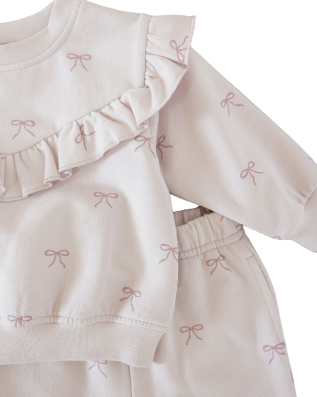 Light pink outfit with ruffled details and embroidered bows on a wooden surface