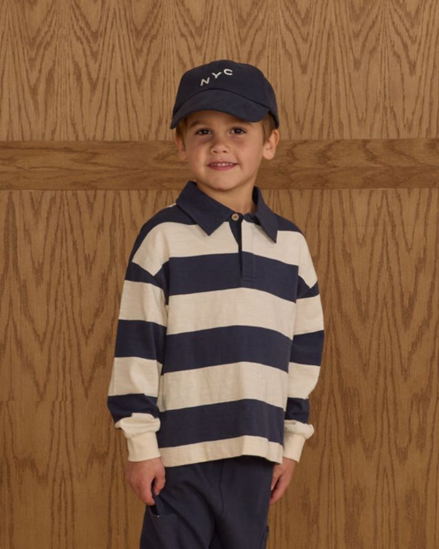 Child wearing a navy and white striped shirt with a matching cap against a wooden background