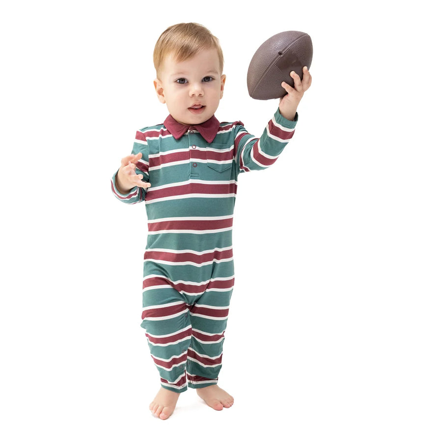 A toddler standing barefoot on a white background, wearing a long-sleeve striped one-piece outfit in teal, burgundy, and white, while holding a brown football.