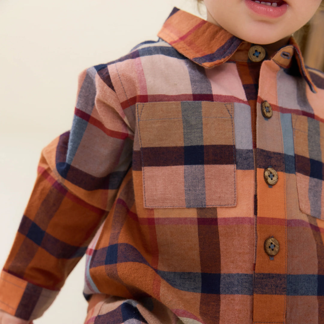 close up of a rust plaid jumpsuit with buttons down the front  and a pocket. 