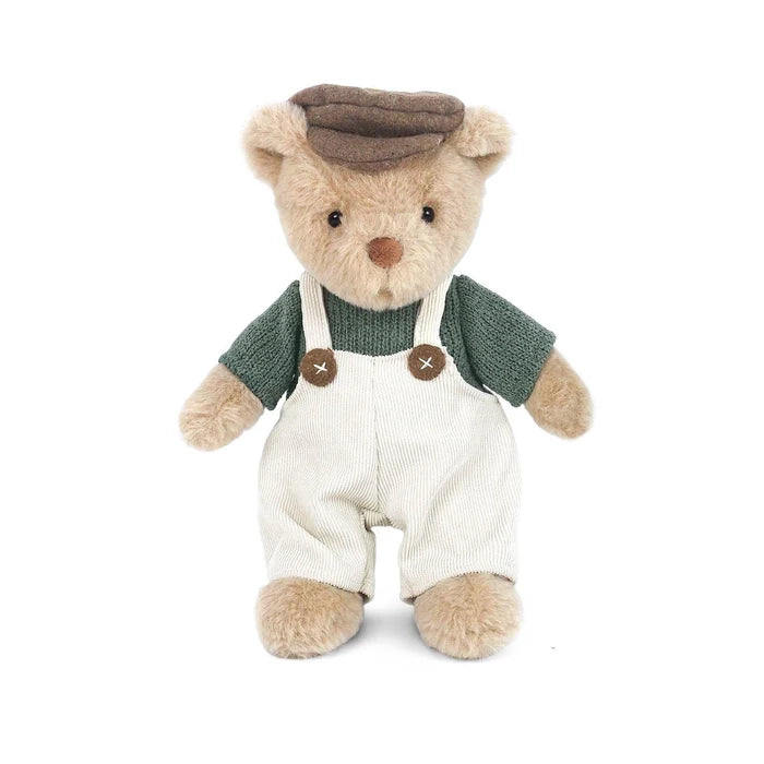 A teddy bear doll wearing a brown flat cap, a dark green knit shirt, and off-white corduroy overalls with brown buttons, photographed against a plain white background.