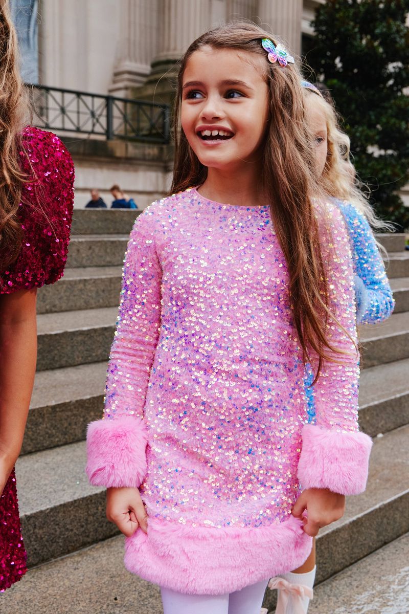 Young girl in a pink sequin dress standing on steps outdoors