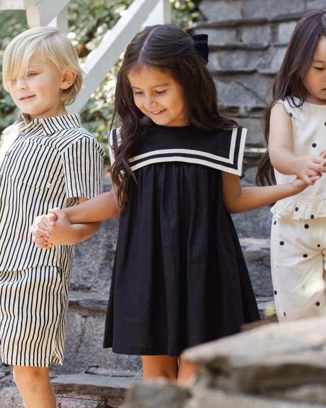 young girl wearing a black sailor dress with oversized bib and white piping. 
