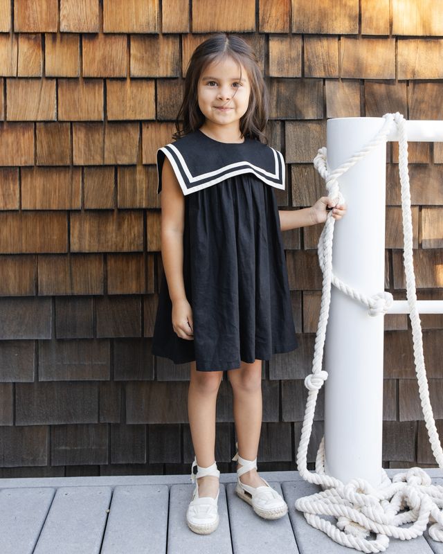 young girl wearing a black sailor dress with white piping standing outdoors. 