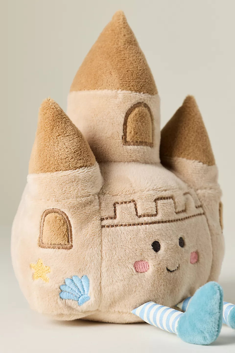 Plush toy sand castle with a face, towers, and a blue anchor on a neutral background