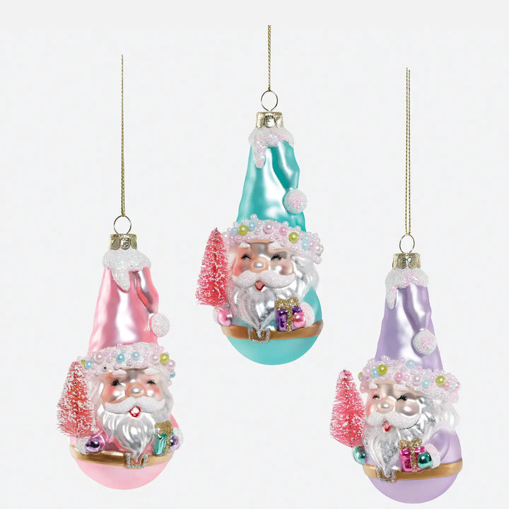 Three Christmas ornament baubles shaped like Santa in pointed hats, shown on a plain light background. One ornament is pink, one is aqua/teal, and one is lavender, each with silver Santa faces, white beards, small trees, and gift boxes.