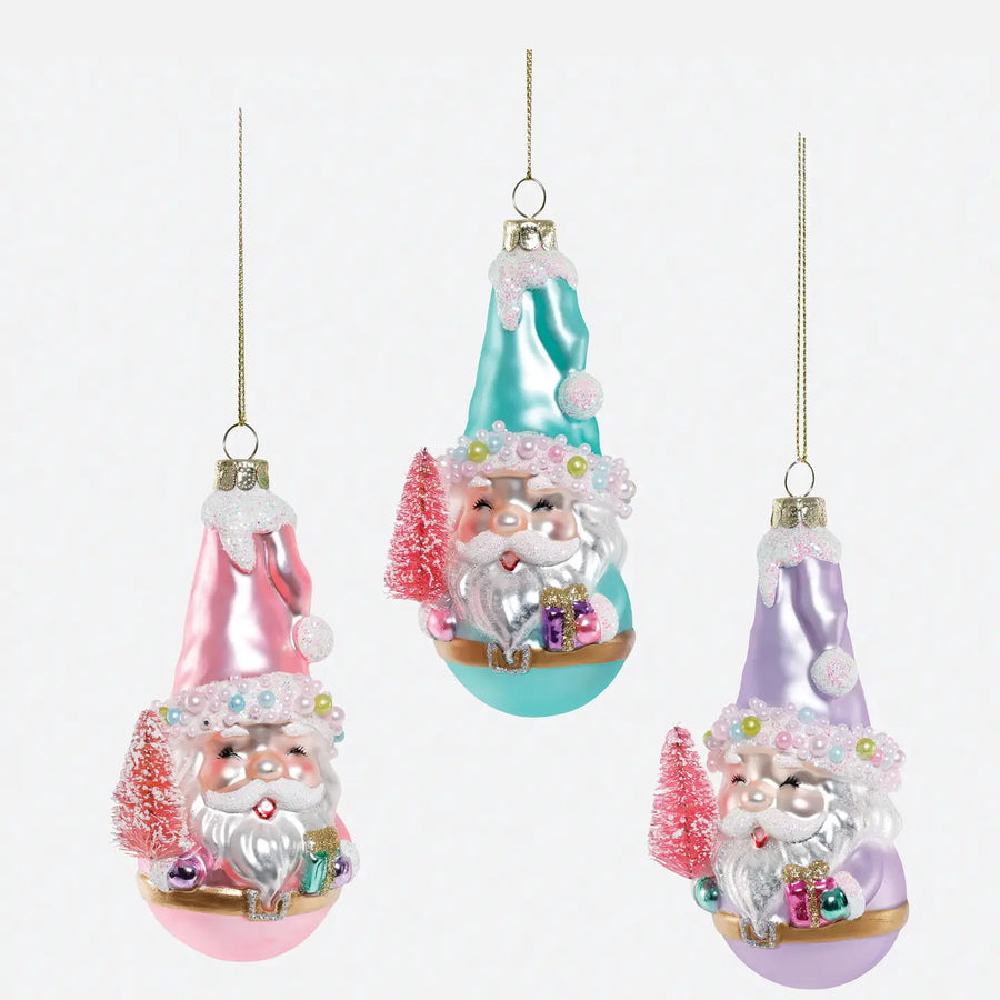 Three Christmas ornament baubles shaped like Santa in pointed hats, shown on a plain light background. One ornament is pink, one is aqua/teal, and one is lavender, each with silver Santa faces, white beards, small trees, and gift boxes.
