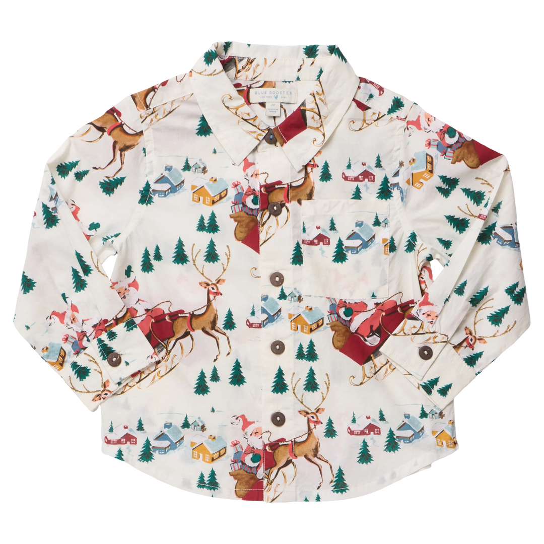 A long-sleeve button-up shirt with a festive Christmas print featuring Santa Claus in red sleighs, brown reindeer, green pine trees, and small houses on an off-white background.