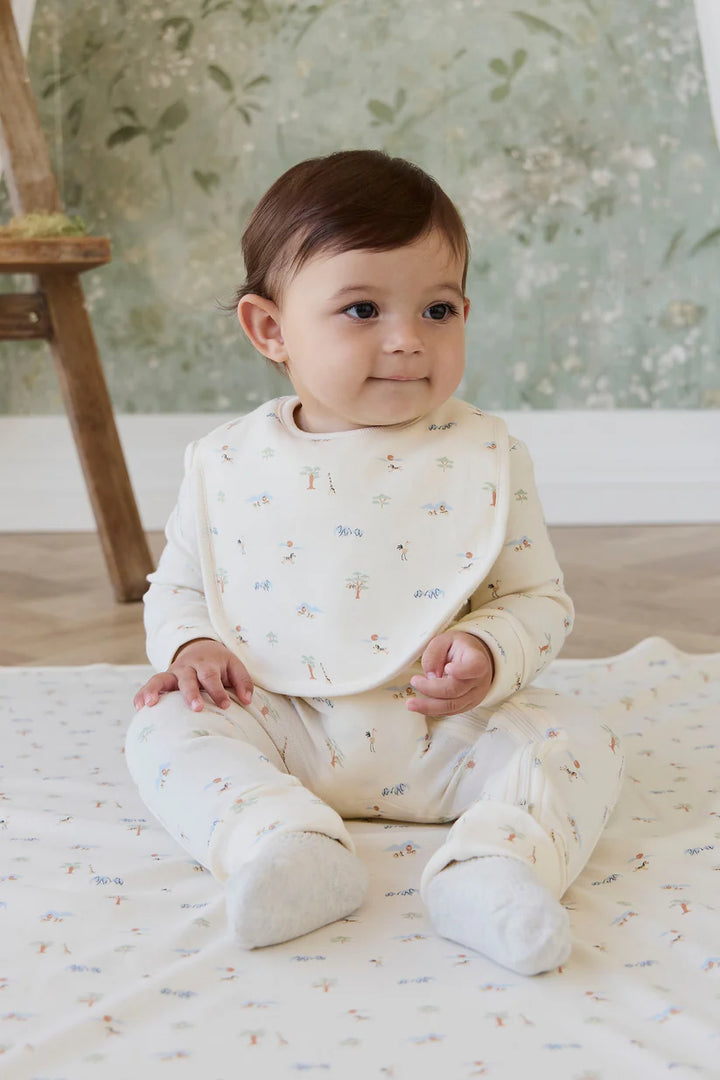 Baby sitting on a white blanket with a Savannah Animal-patterned wall in the background
