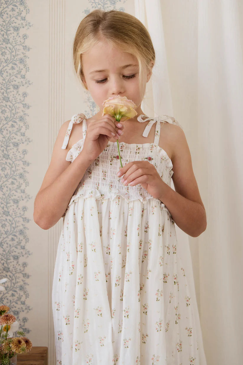 Young girl in a floral dress smelling a flower against a neutral background