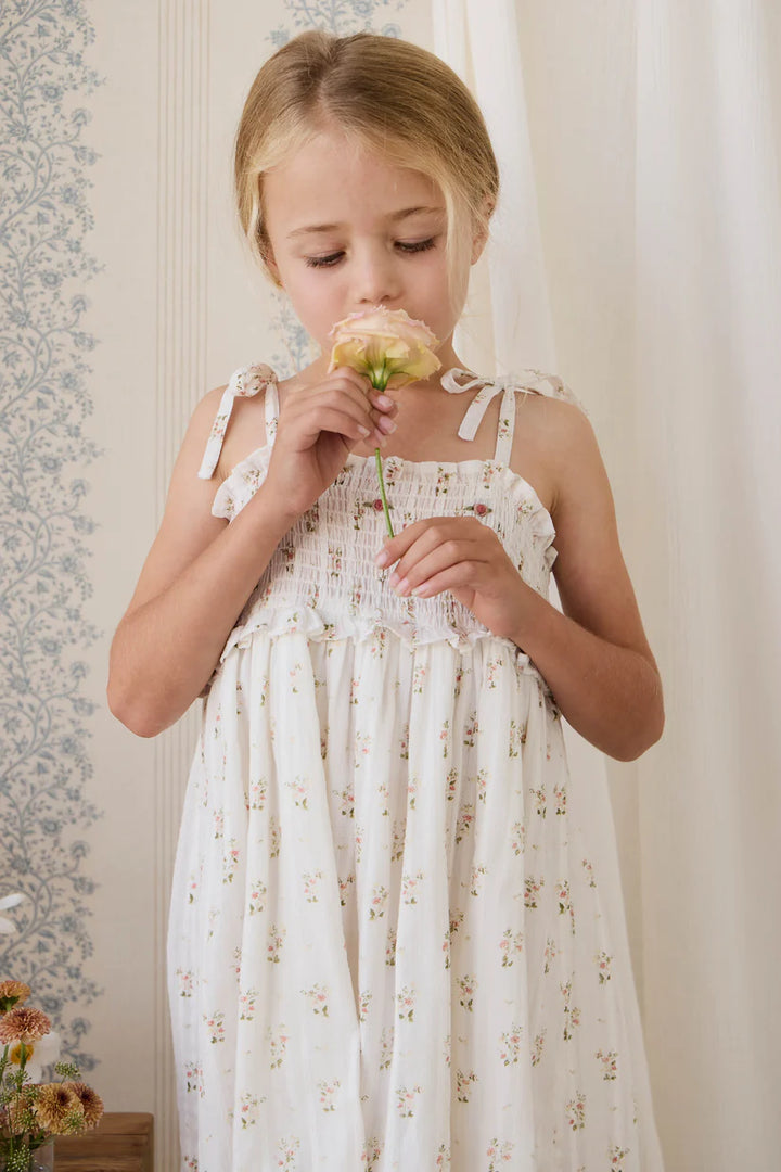 Young girl in a floral dress smelling a flower against a neutral background