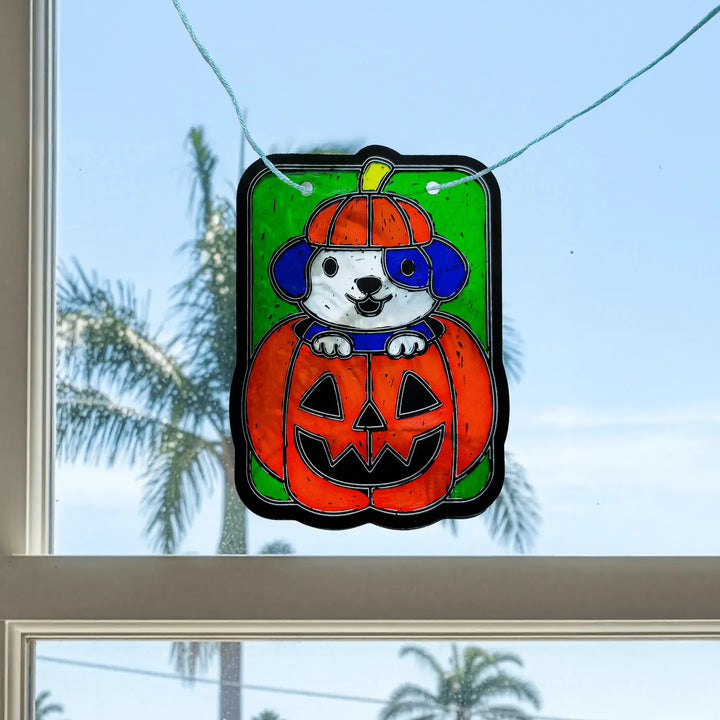 Decorative window cling of a dog in a pumpkin costume with a green background.