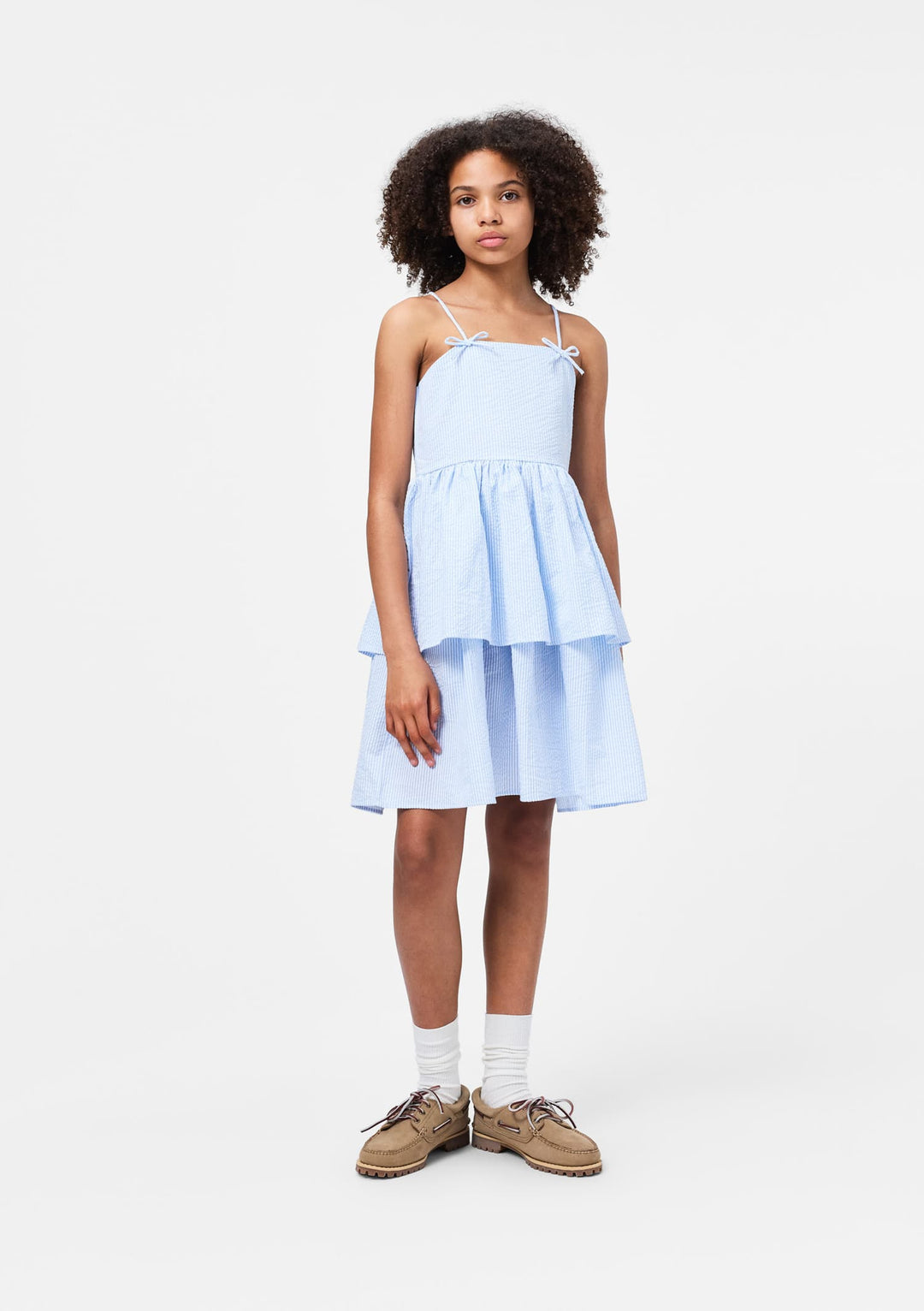 Young girl wearing a light blue seersucker dress on a white background