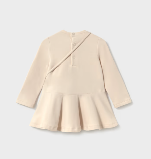 A cream-colored long-sleeve baby dress shown from the back, featuring a wrap-style back closure with three buttons and a flared peplum hem, set against a light gray background.