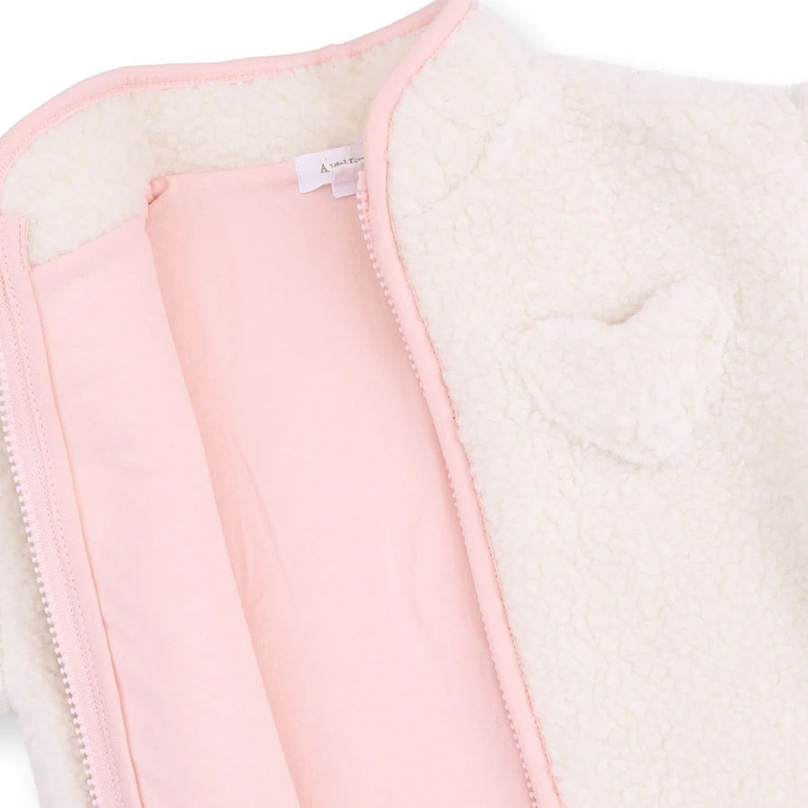 Close-up of a cream sherpa fleece jacket with a light pink lining and zipper, featuring a heart-shaped applique on the chest.