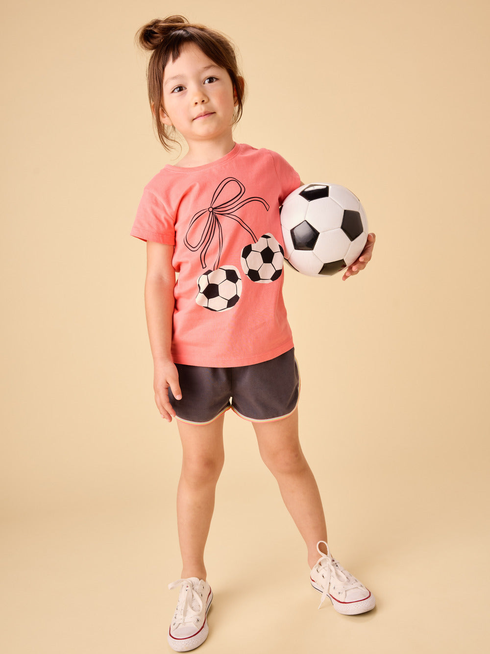 young girl wearing a peach tee with soccer ball cherries tied with a bow