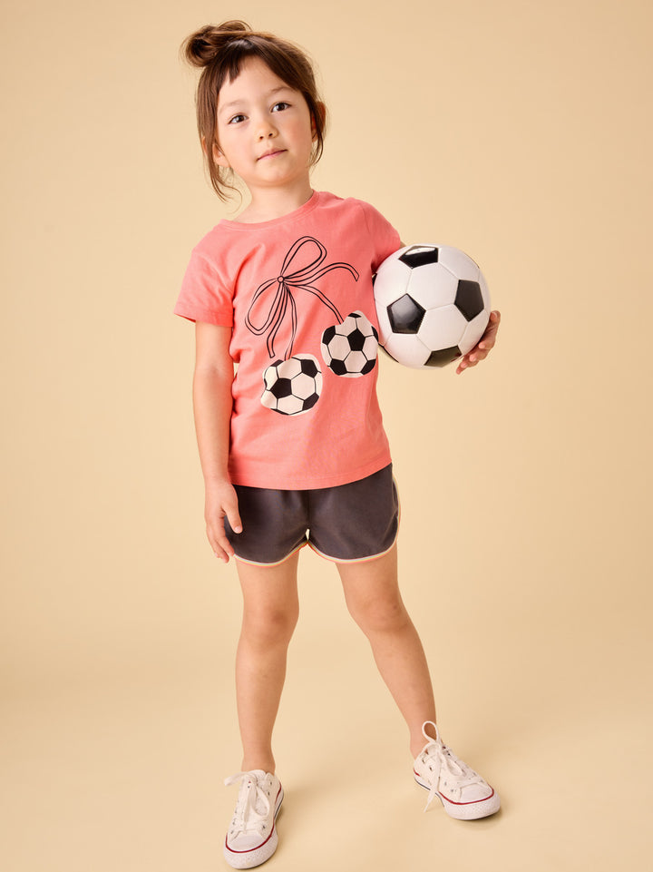 young girl wearing a peach tee with soccer ball cherries tied with a bow