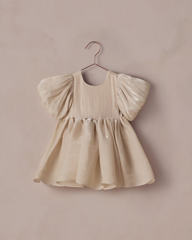 Beige baby dress with puff sleeves on a hanger against a beige background