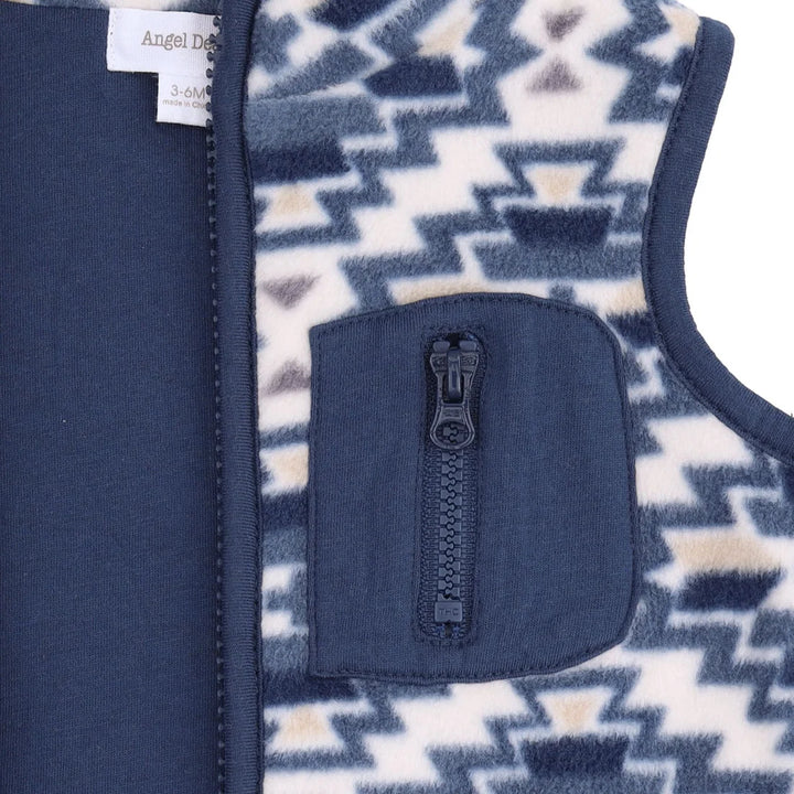 Close-up of a children's fleece vest showing a navy blue zipper pocket with a black zipper, a patterned side panel in navy, cream, and tan, and a solid navy fabric panel on the other side.