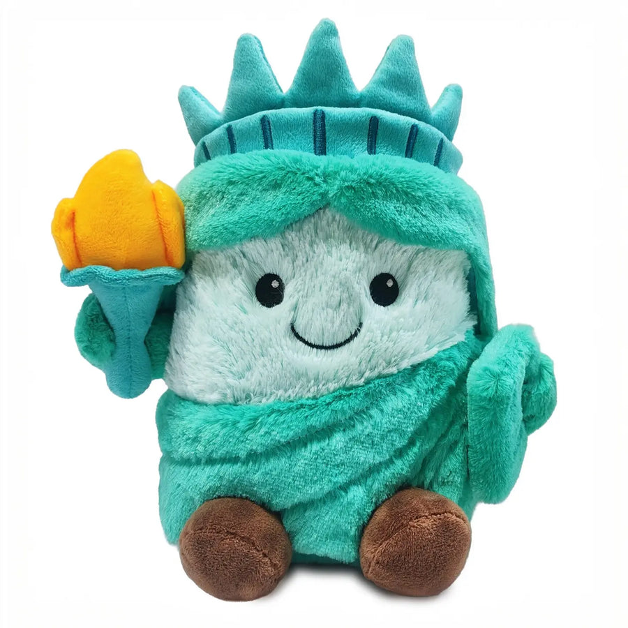 A plush toy shaped like a cartoon Statue of Liberty character, wearing a teal crown and robe with a white face, holding a yellow torch, on a plain white background.