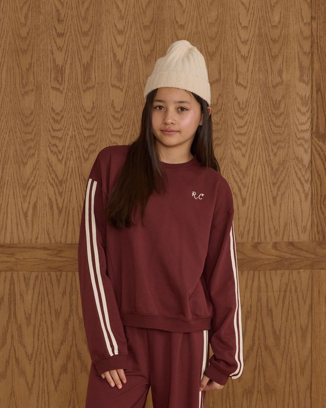 Girl wearing a burgundy tracksuit with white stripes against a wooden background