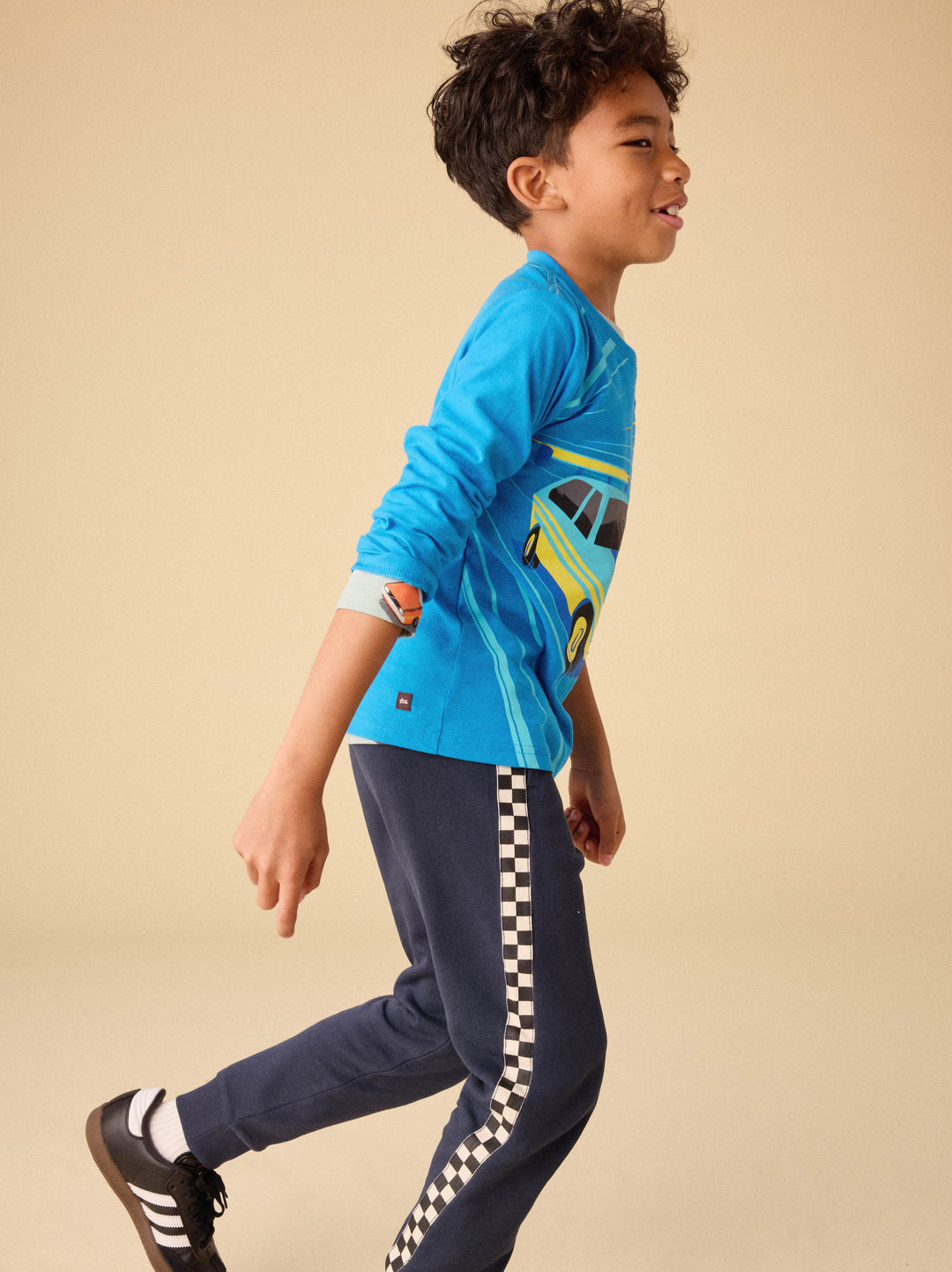 Child wearing a blue long-sleeve shirt with a car design and navy pants with checkered stripes on a beige background